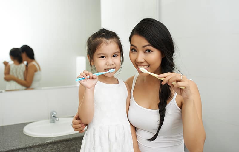 A mother and a daughter brushing teeth together in a bathroom